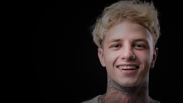 Portrait eines jungen Mannes mit Tattoos vor dunklem Hintergrund