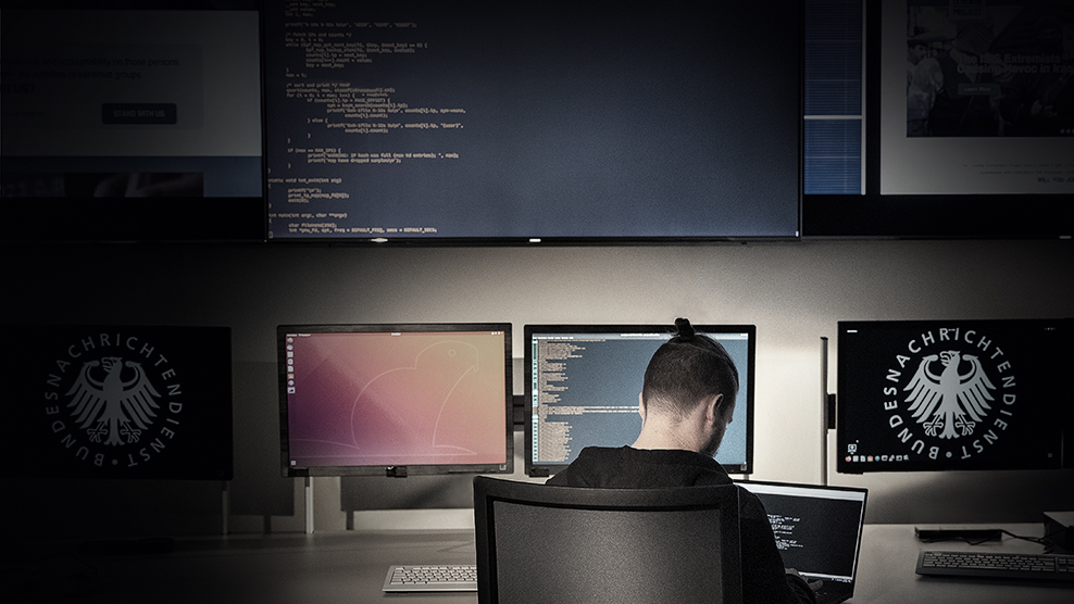 Hacker der an einem Laptop in einem Raum mit vielen Bildschirmen arbeitet